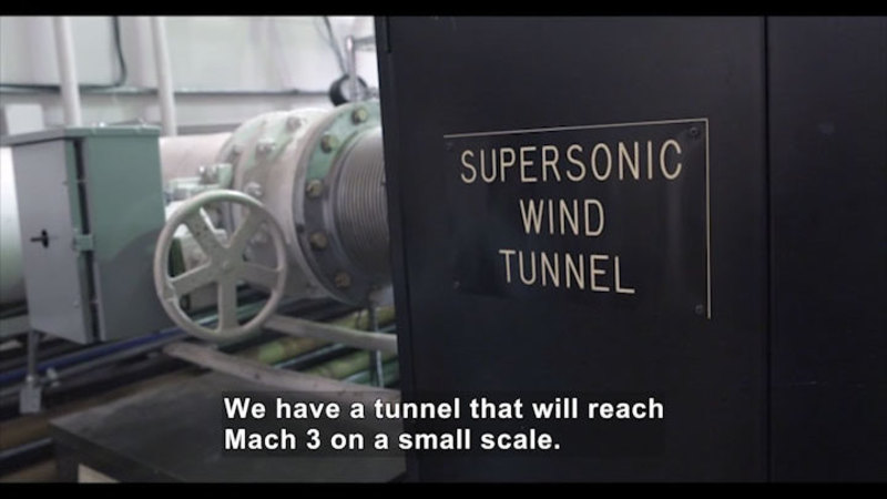 Cylindrical metal duct with a control box and large valve control. Sign on wall says Supersonic Wind Tunnel. Caption: We have a tunnel that will reach Mach 3 on a small scale.